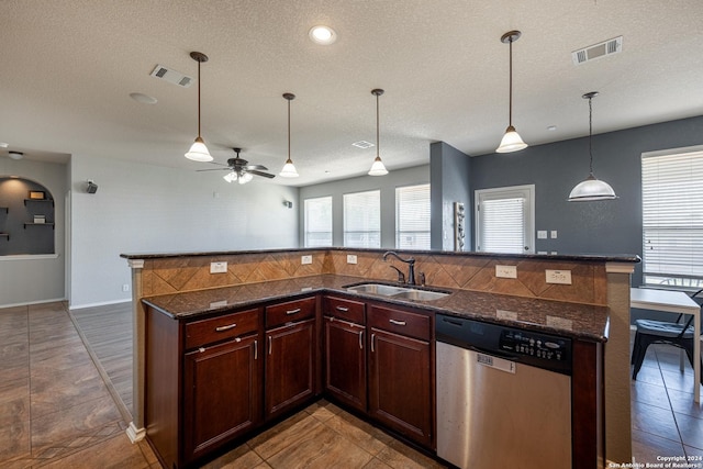 kitchen featuring a textured ceiling, dishwasher, hanging light fixtures, sink, and a center island with sink