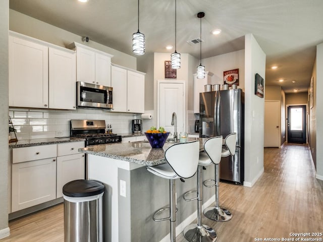 kitchen with white cabinets, stainless steel appliances, a center island with sink, and pendant lighting