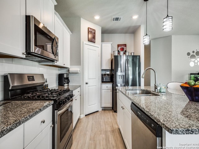 kitchen featuring appliances with stainless steel finishes, hanging light fixtures, a kitchen island with sink, white cabinets, and sink