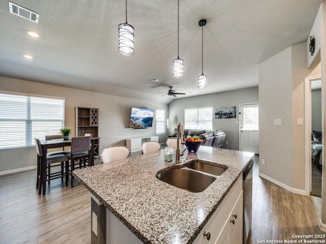 kitchen featuring pendant lighting, sink, white cabinets, light stone counters, and an island with sink