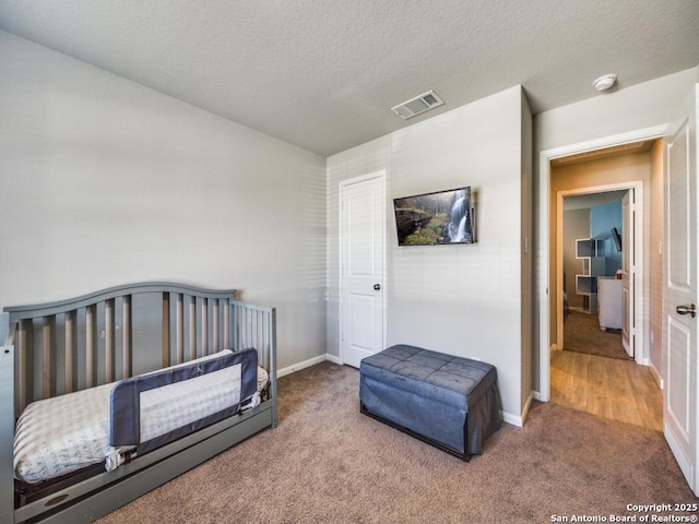 carpeted bedroom featuring a nursery area and a textured ceiling