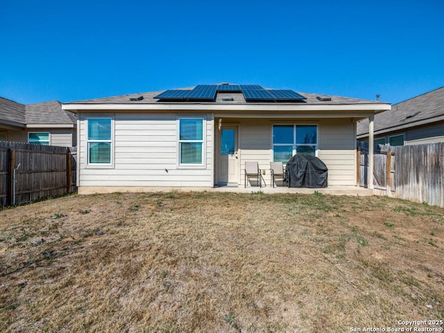 back of house featuring a patio area, a yard, and solar panels