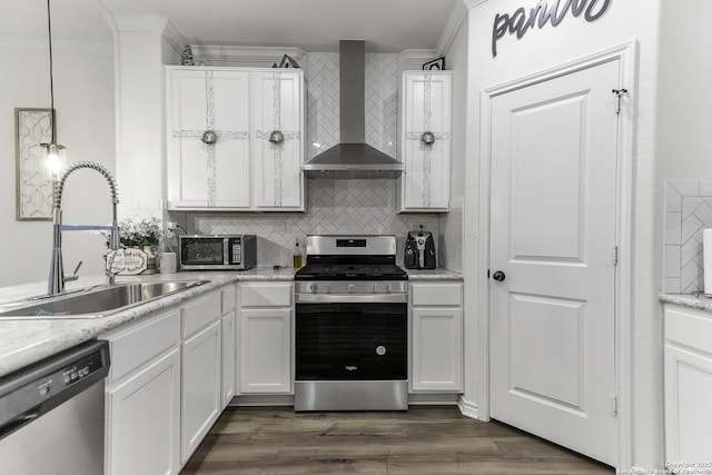 kitchen featuring appliances with stainless steel finishes, white cabinetry, sink, decorative light fixtures, and wall chimney exhaust hood