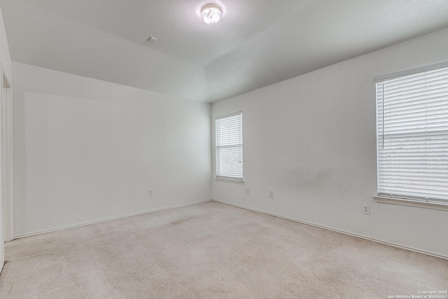 empty room with light colored carpet, a textured ceiling, and vaulted ceiling