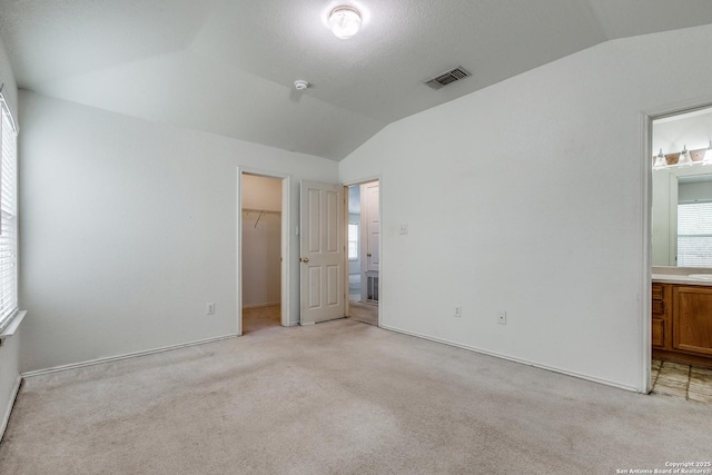 unfurnished bedroom featuring light carpet, a closet, lofted ceiling, and a walk in closet