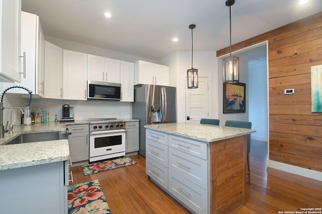 kitchen featuring appliances with stainless steel finishes, tasteful backsplash, wood-type flooring, white cabinets, and decorative light fixtures