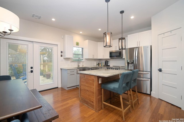 kitchen featuring white cabinetry, stainless steel appliances, a kitchen island, and decorative light fixtures