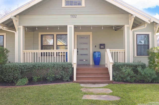 view of exterior entry with covered porch and a lawn