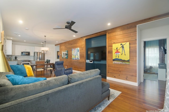 living room with ceiling fan, wood walls, and dark hardwood / wood-style flooring