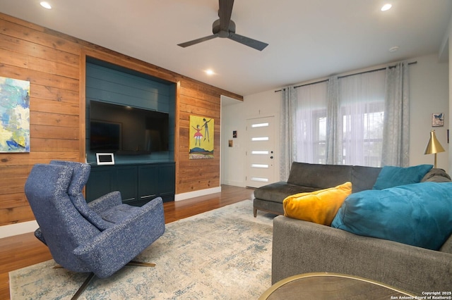 living room featuring wood-type flooring, wooden walls, and ceiling fan