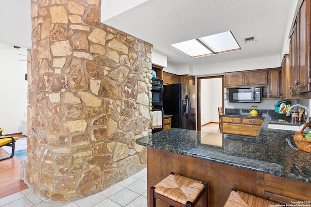 kitchen featuring a textured ceiling, black appliances, a skylight, sink, and kitchen peninsula