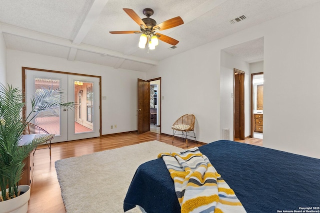 bedroom with ceiling fan, french doors, a textured ceiling, connected bathroom, and beamed ceiling