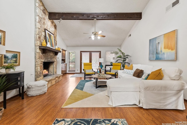 living room featuring hardwood / wood-style floors, a textured ceiling, a fireplace, vaulted ceiling with beams, and ceiling fan