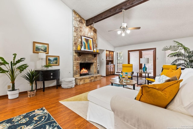 living room with a textured ceiling, wood-type flooring, a fireplace, vaulted ceiling with beams, and ceiling fan