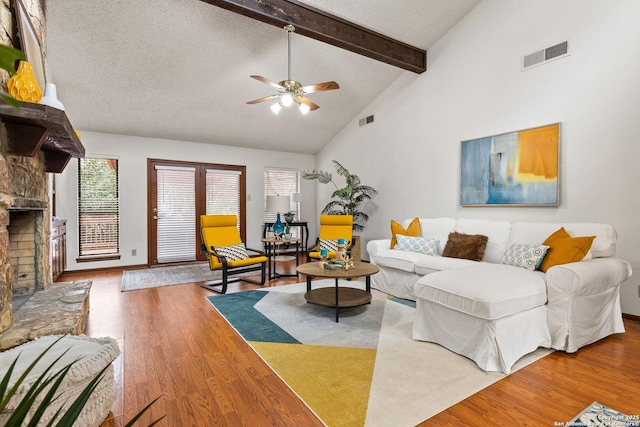 living room featuring a stone fireplace, beam ceiling, a textured ceiling, and wood-type flooring