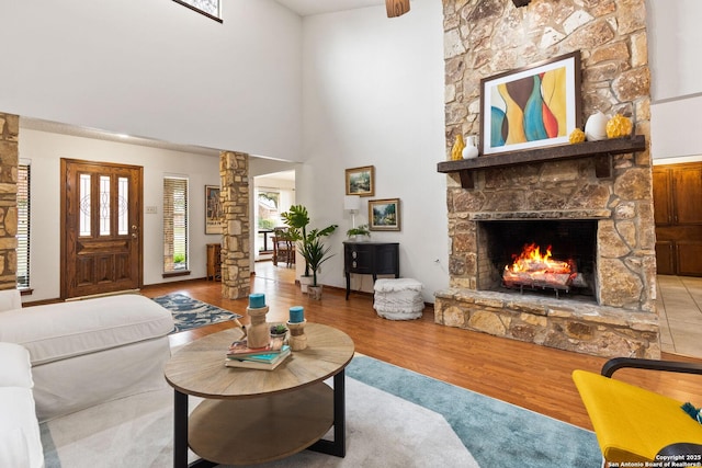 living room featuring hardwood / wood-style flooring, a stone fireplace, ornate columns, and plenty of natural light