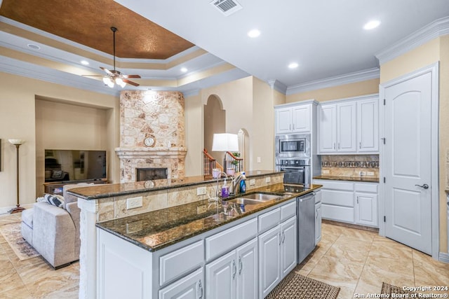 kitchen with white cabinets, stainless steel appliances, dark stone countertops, ornamental molding, and a kitchen island with sink