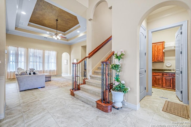 entryway with crown molding, ceiling fan, and a raised ceiling