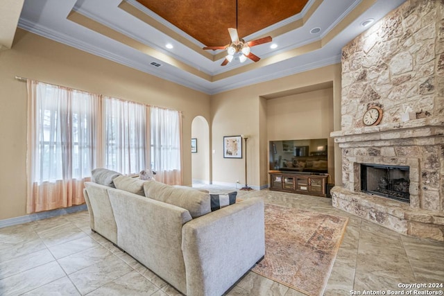 living room featuring a fireplace, a high ceiling, a raised ceiling, ornamental molding, and ceiling fan