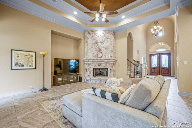 living room with ornamental molding, ceiling fan with notable chandelier, a stone fireplace, and a raised ceiling