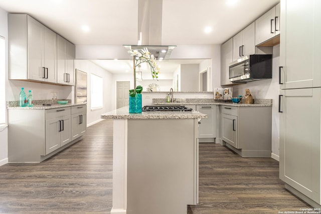 kitchen with dark wood-type flooring, light stone counters, a kitchen island, island range hood, and stainless steel appliances