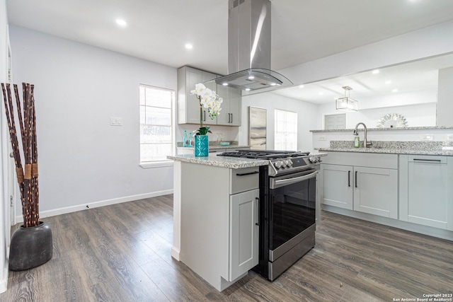 kitchen with light stone countertops, stainless steel gas range, dark hardwood / wood-style flooring, island exhaust hood, and gray cabinetry