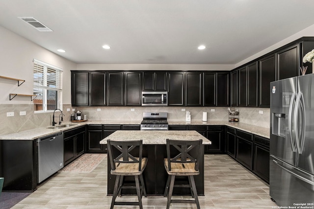 kitchen with appliances with stainless steel finishes, tasteful backsplash, sink, a kitchen island, and light wood-type flooring