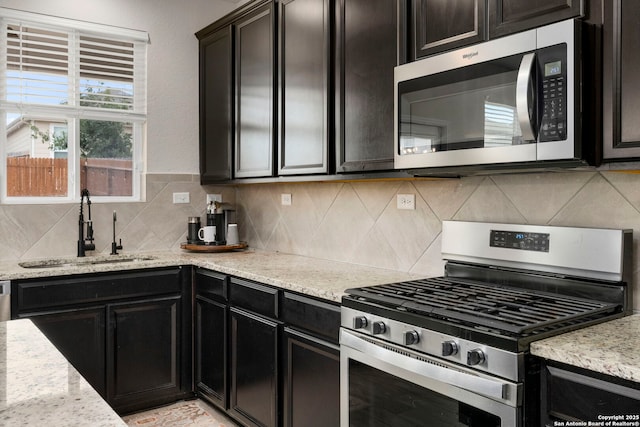 kitchen with sink, stainless steel appliances, light stone countertops, and backsplash