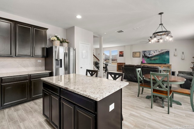 kitchen featuring a kitchen island, tasteful backsplash, hanging light fixtures, stainless steel fridge with ice dispenser, and light wood-type flooring