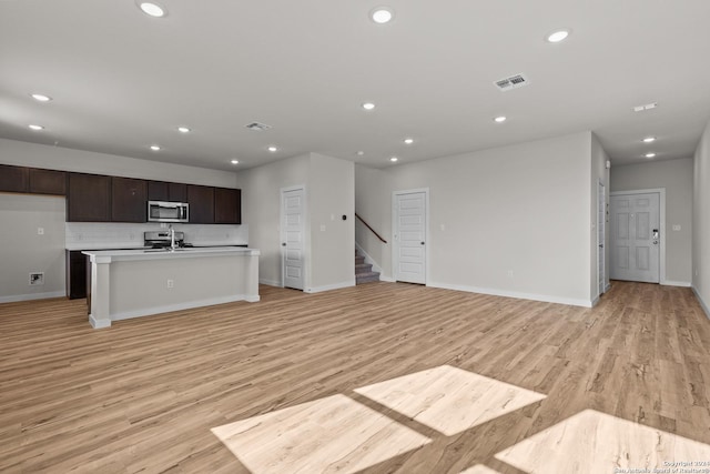 kitchen featuring light hardwood / wood-style floors, sink, decorative backsplash, a center island with sink, and dark brown cabinets