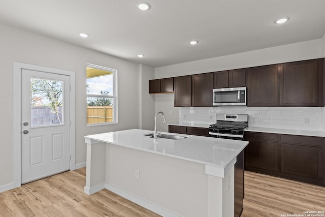 kitchen featuring appliances with stainless steel finishes, sink, light wood-type flooring, a center island with sink, and decorative backsplash