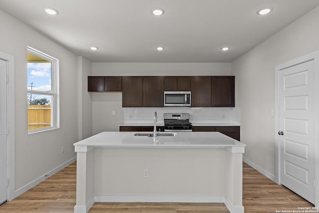 kitchen with appliances with stainless steel finishes, light hardwood / wood-style floors, sink, backsplash, and a kitchen island with sink