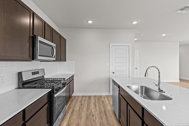 kitchen featuring light stone countertops, tasteful backsplash, sink, light hardwood / wood-style flooring, and stainless steel appliances