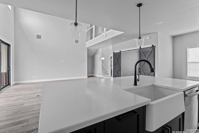 kitchen with light hardwood / wood-style floors, a barn door, hanging light fixtures, stainless steel dishwasher, and sink