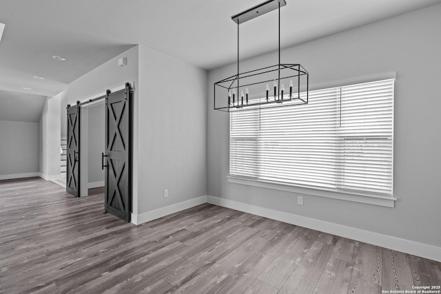 unfurnished dining area featuring a barn door, light hardwood / wood-style floors, and lofted ceiling