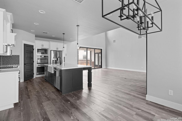 kitchen with a kitchen island with sink, decorative backsplash, white cabinets, decorative light fixtures, and stainless steel appliances