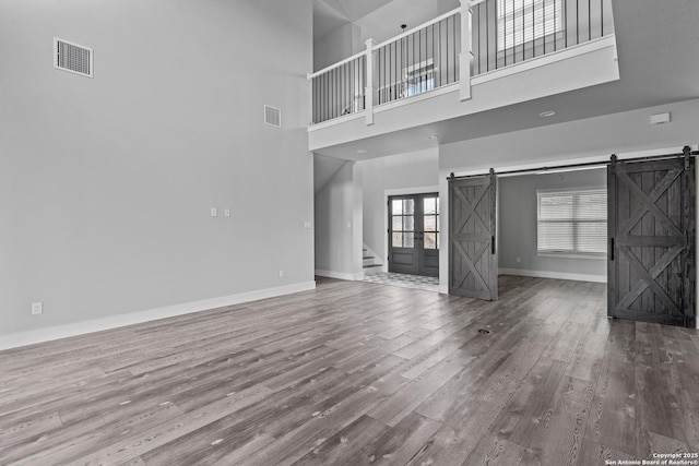 unfurnished living room featuring hardwood / wood-style flooring, a towering ceiling, and a barn door