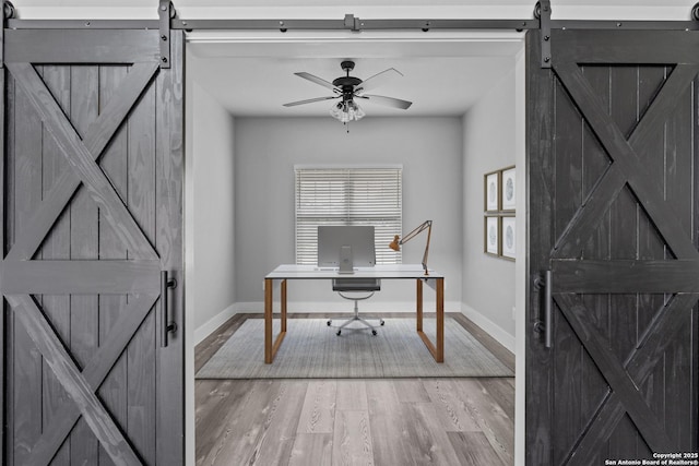 office featuring ceiling fan, wood-type flooring, and a barn door