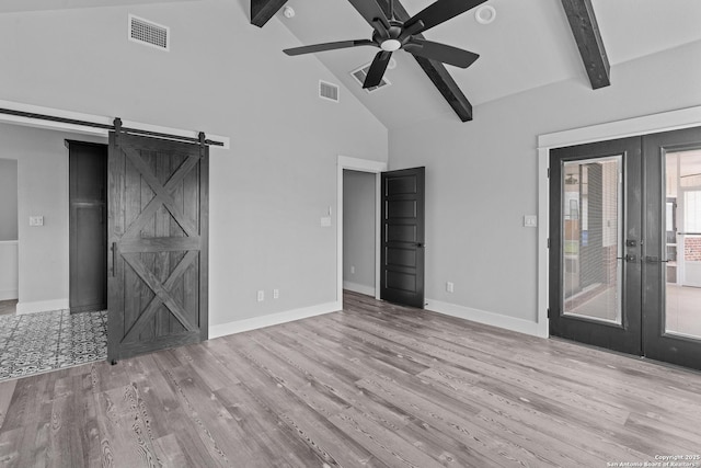 empty room featuring french doors, light wood-type flooring, ceiling fan, beam ceiling, and a barn door