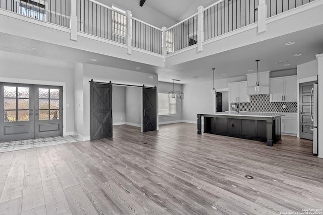 unfurnished living room with a high ceiling, french doors, sink, light hardwood / wood-style flooring, and a barn door