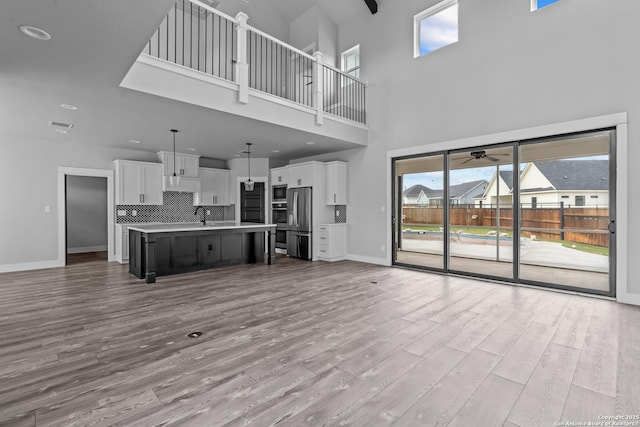 unfurnished living room with light wood-type flooring, a towering ceiling, and ceiling fan