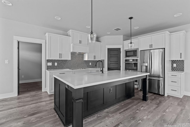 kitchen featuring a kitchen island with sink, pendant lighting, white cabinetry, and appliances with stainless steel finishes