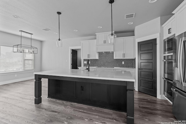 kitchen with white cabinetry, a kitchen island with sink, pendant lighting, and appliances with stainless steel finishes