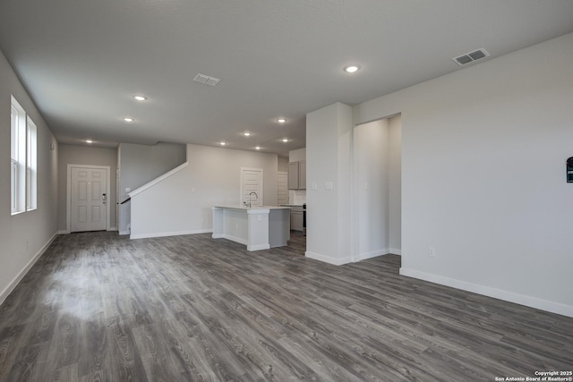 unfurnished living room featuring dark wood-style floors, baseboards, stairway, and visible vents