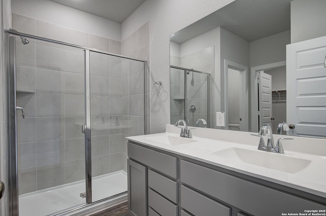 full bath with double vanity, a shower stall, a spacious closet, and a sink