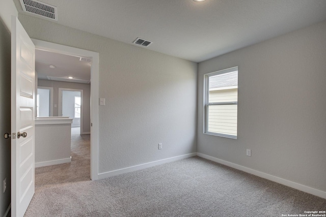 spare room featuring attic access, carpet flooring, visible vents, and baseboards