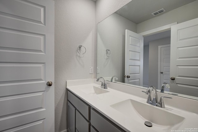 full bathroom featuring a textured wall, visible vents, a sink, and double vanity