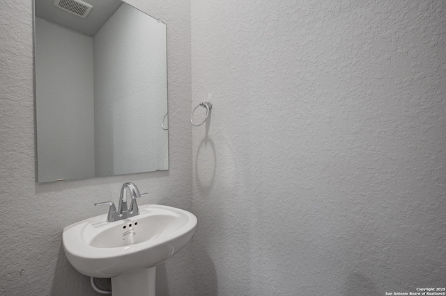 bathroom with visible vents, a sink, and a textured wall