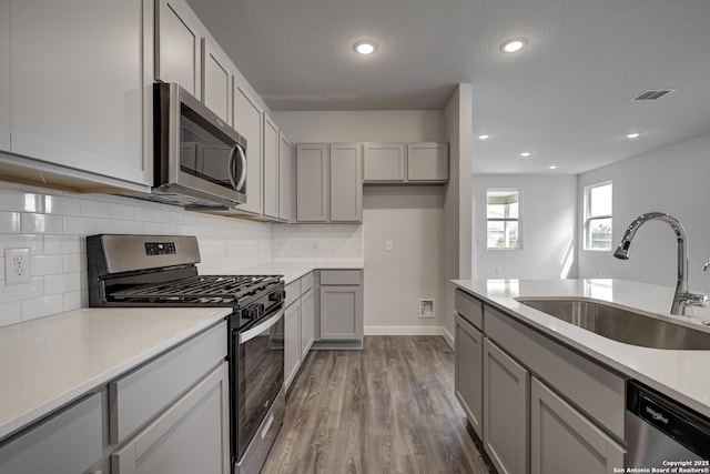 kitchen with dark wood-style floors, stainless steel appliances, tasteful backsplash, gray cabinets, and a sink