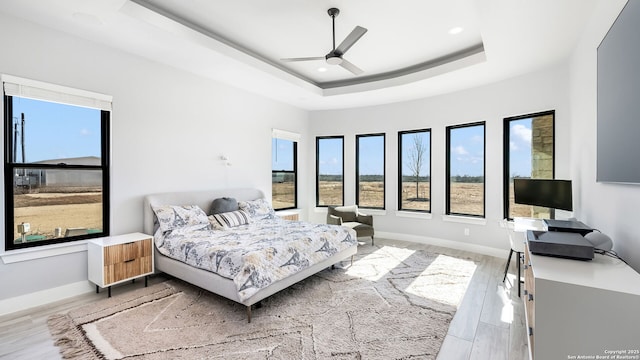 bedroom with light wood-type flooring, ceiling fan, and a raised ceiling